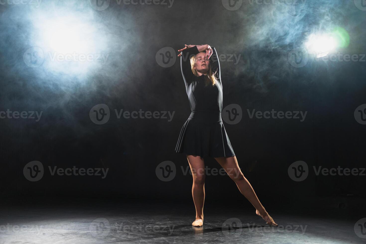 Contemporary woman dancer posing on black background with smoke. Adult female artist performer dancing with expression. Modern ballerina dancing in darkness. Passion dance in dark. Flexibility balance photo