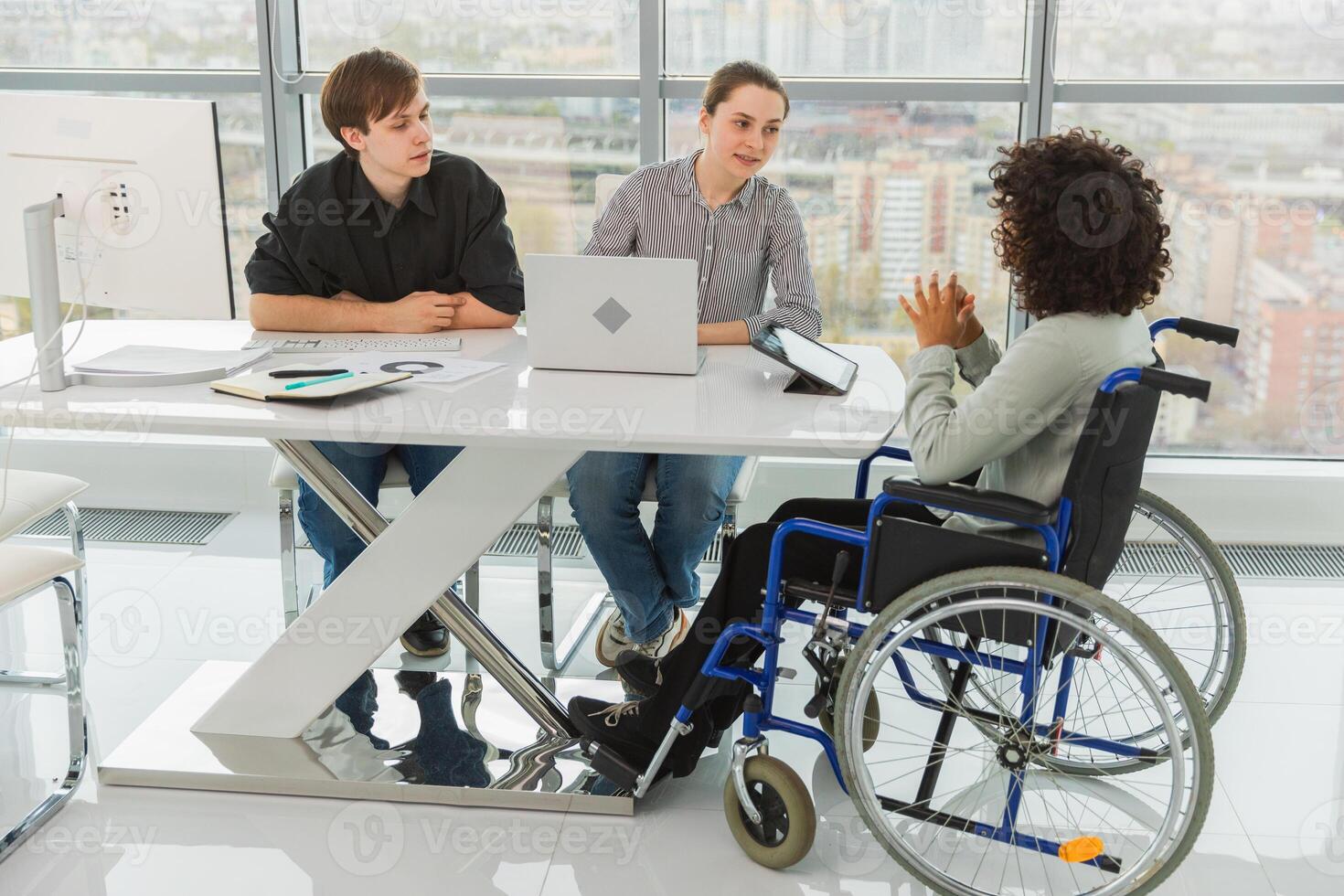 Teamwork brainstorm. Diverse multiracial colleagues woman in chair for people with disability working together. Group of people sitting in creative office discussing business. Young professional team photo