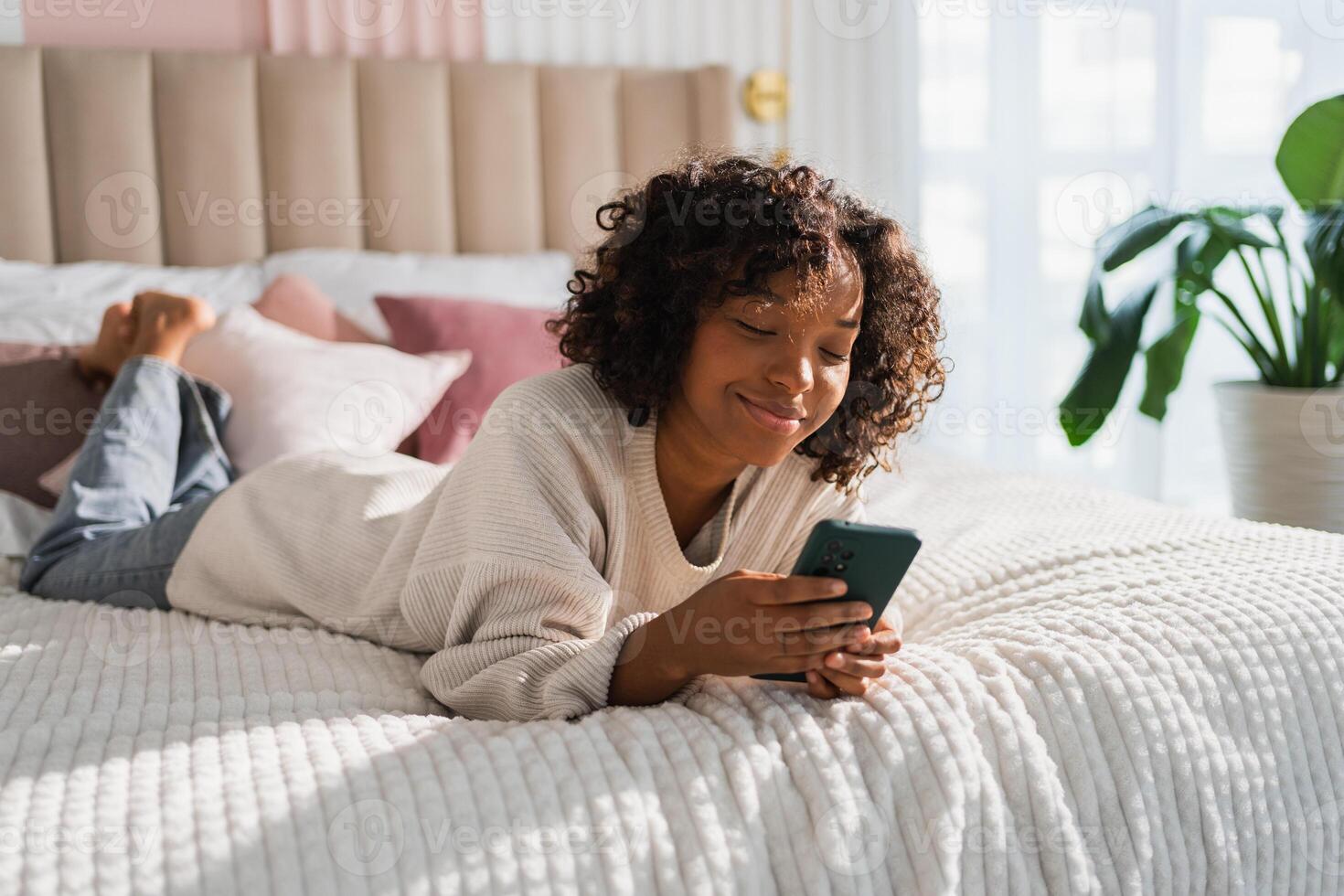 African girl holding smartphone touch screen typing scroll page at home. Woman with cell phone surfing internet using social media apps playing game. Shopping online Internet news cellphone addiction photo