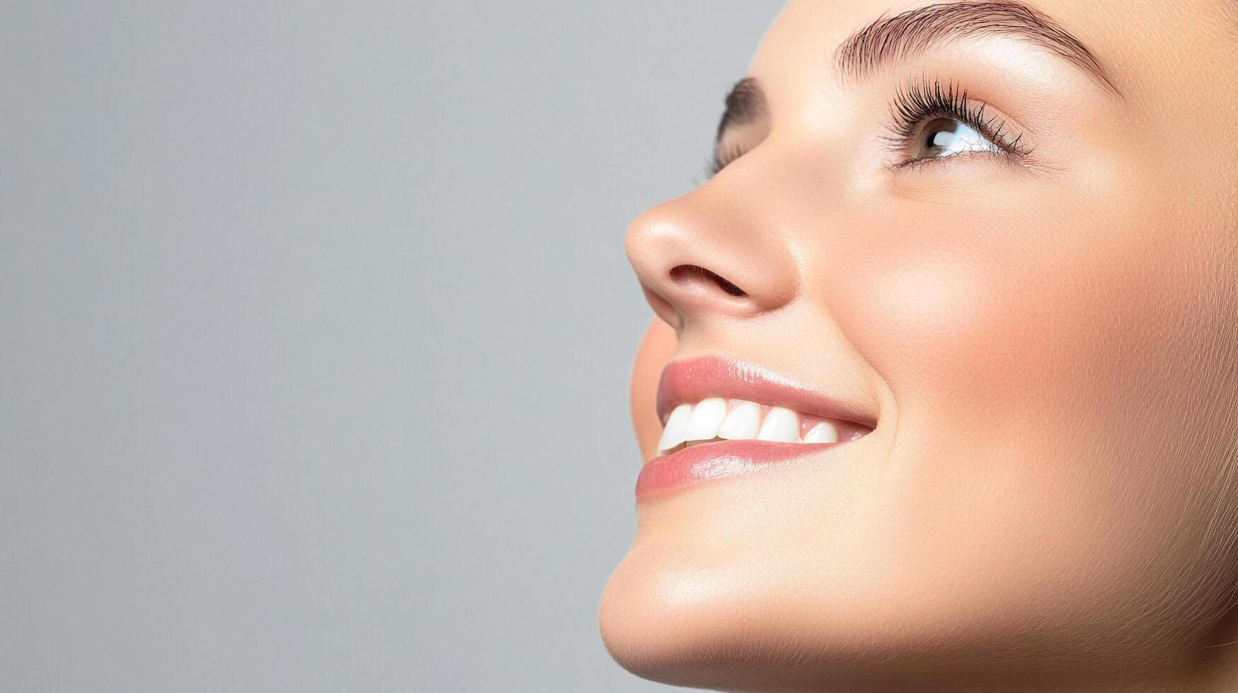 Portrait of a fair-skinned woman with a radiant smile, looking upwards with a positive expression, showcasing elegant beauty on a grey background. photo