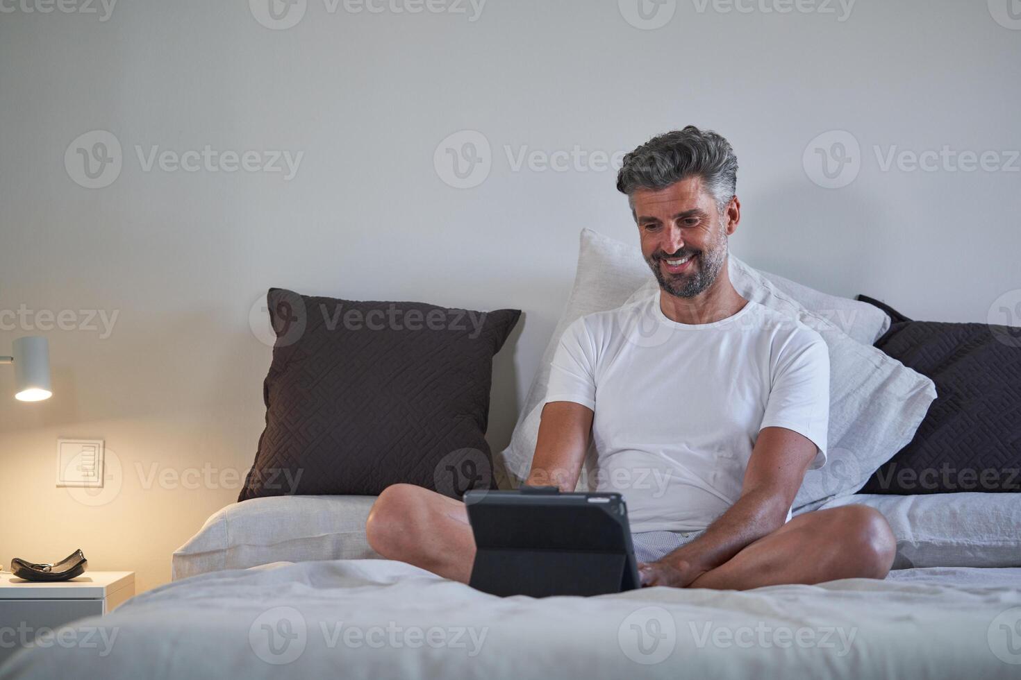 Cheerful businessman browsing tablet in bed photo