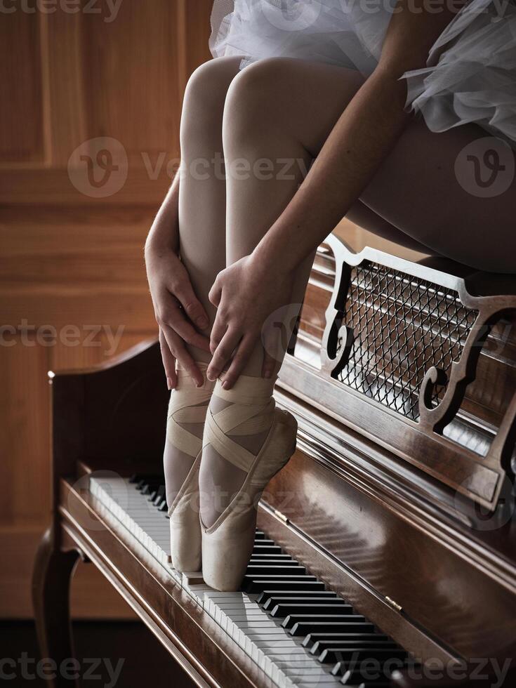 Crop ballerina sitting on piano and pushing keys with feet photo