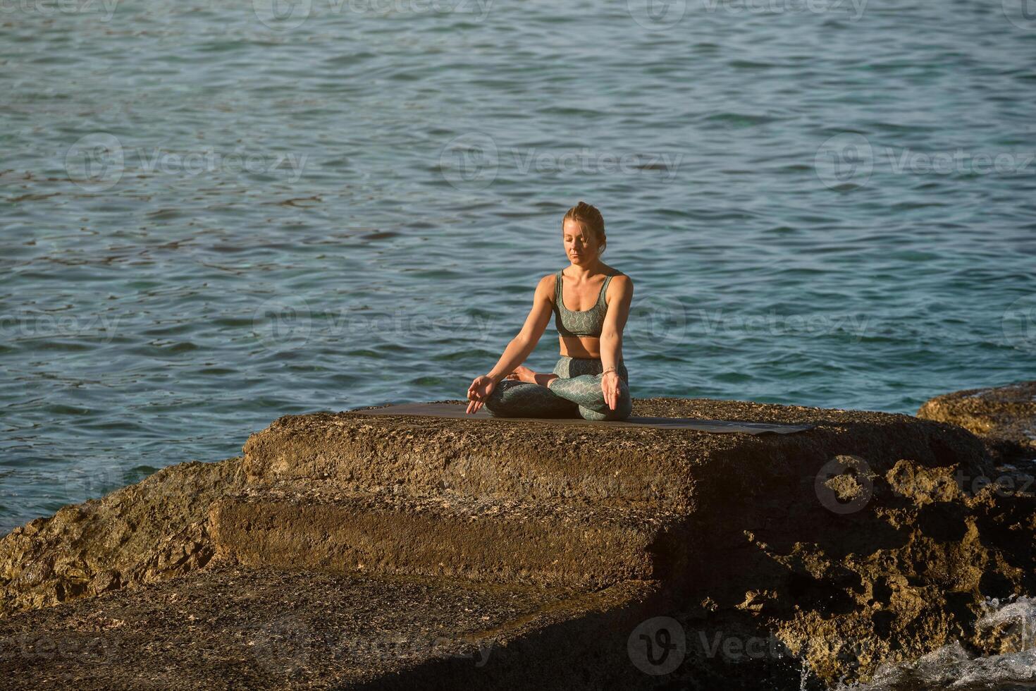 Calm woman meditating on stone at seaside photo
