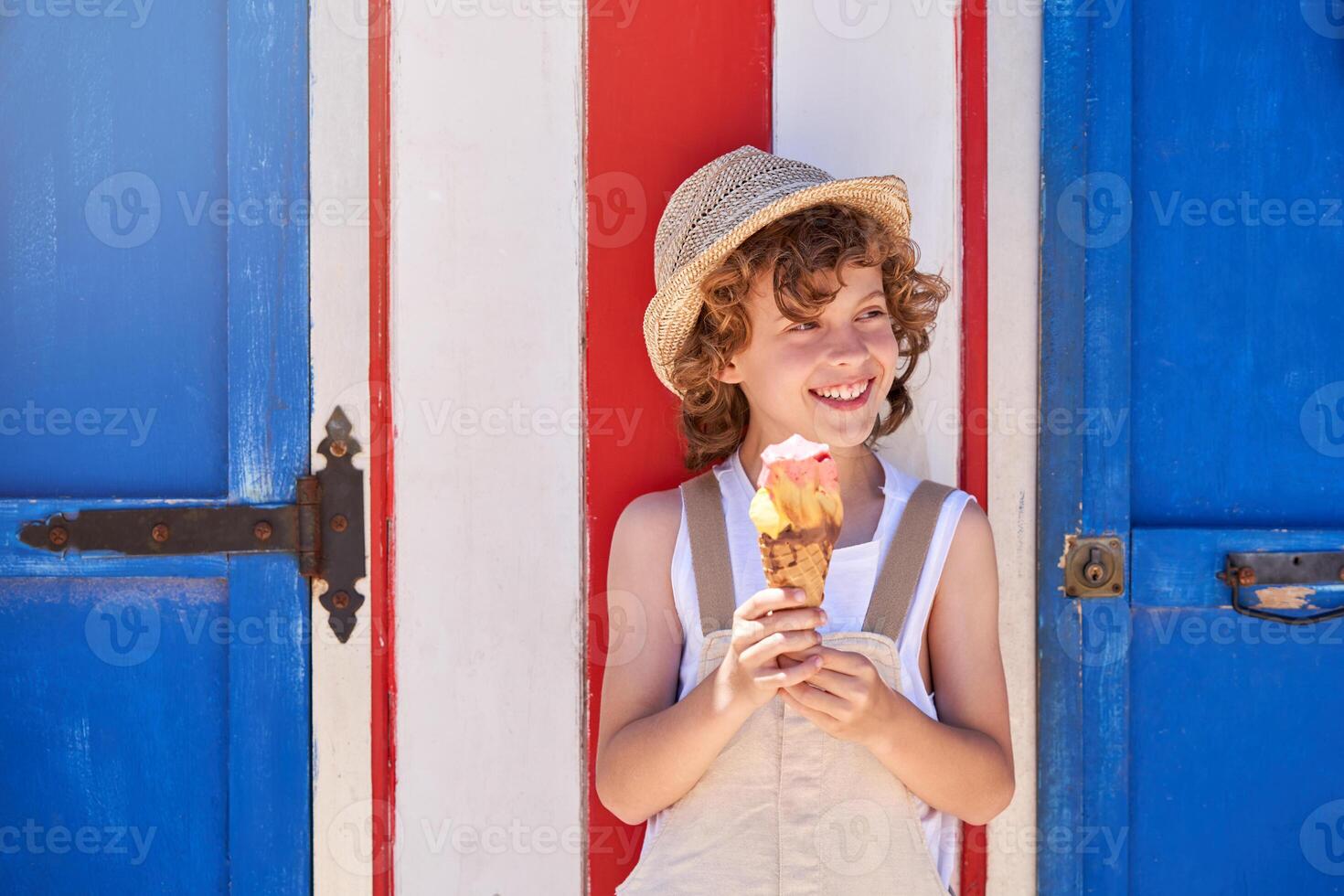 Cheerful boy in straw hat with ice cream near blue door photo