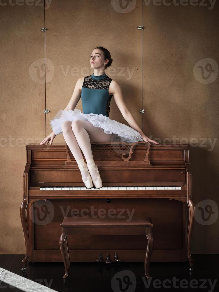 Slender ballerina in tutu and pointe shoes sitting on piano photo