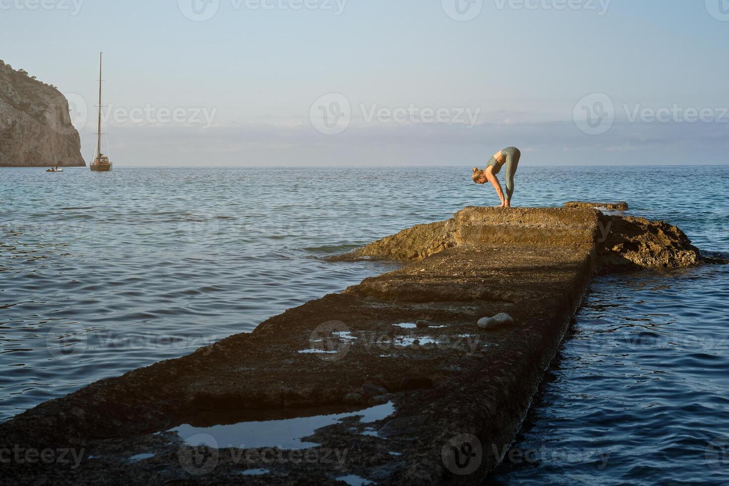 Woman practicing yoga on stone pier at sea photo