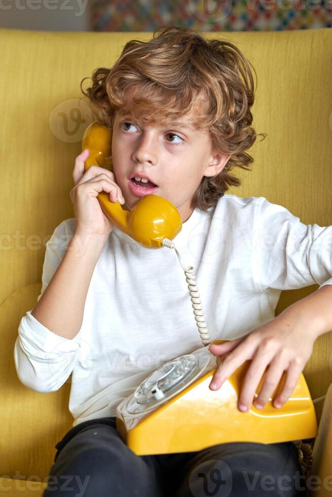 Pensive boy talking on retro telephone in room photo