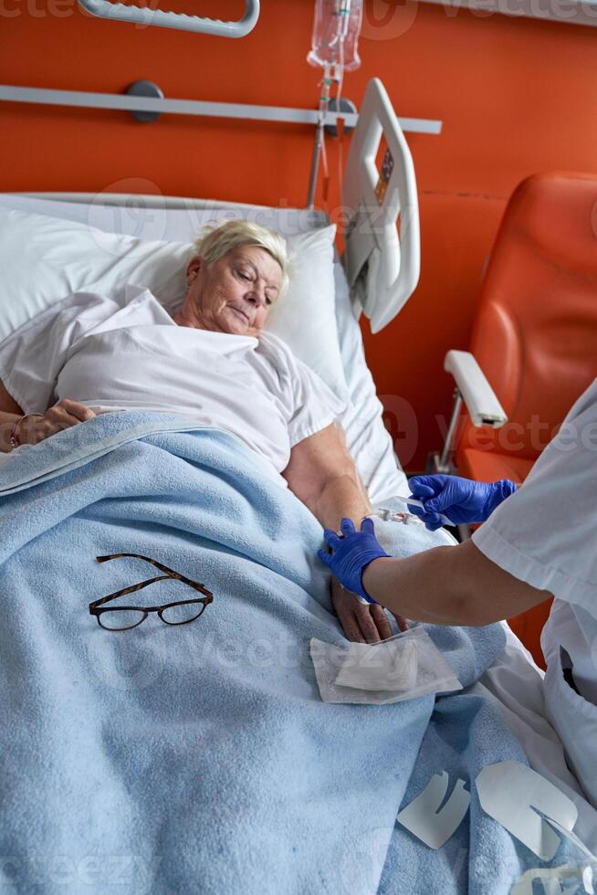 Unrecognizable nurse doing intravenous injection to aged female photo