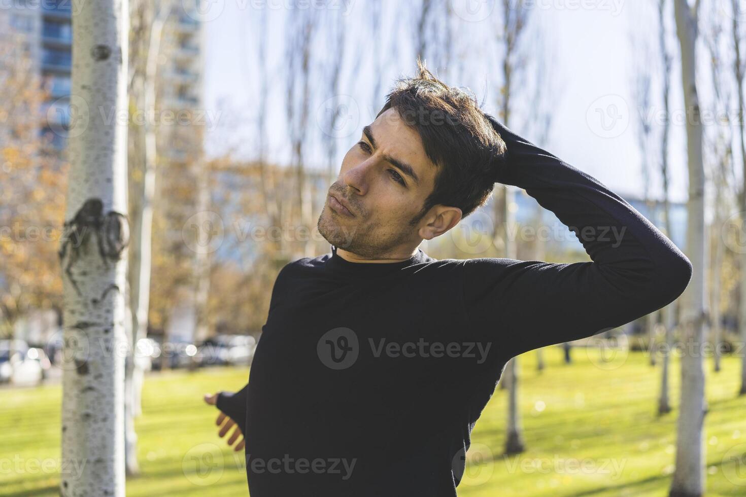 Sporty handsome man stretching neck and head after jogging in city public park photo