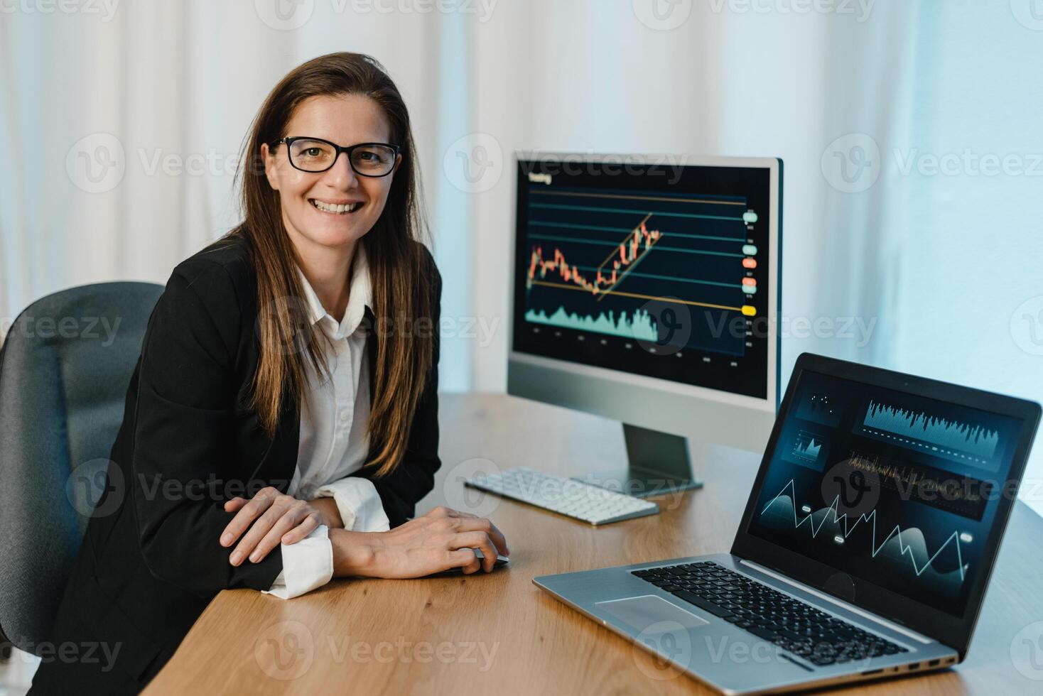 Female trader at table with laptop and computer monitor photo