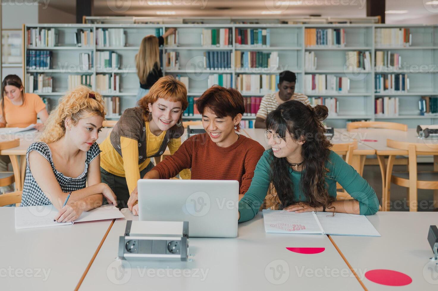 Happy diverse groupmates using laptop and smiling while doing task in library photo