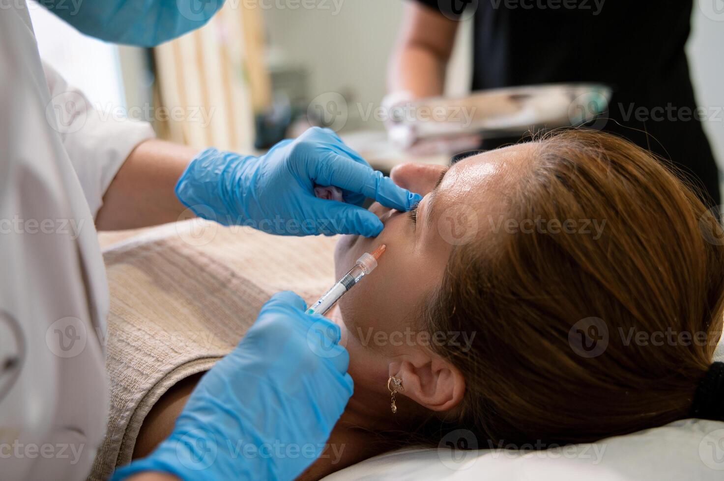 Anonymous beautician administering injection to cheek of female client photo