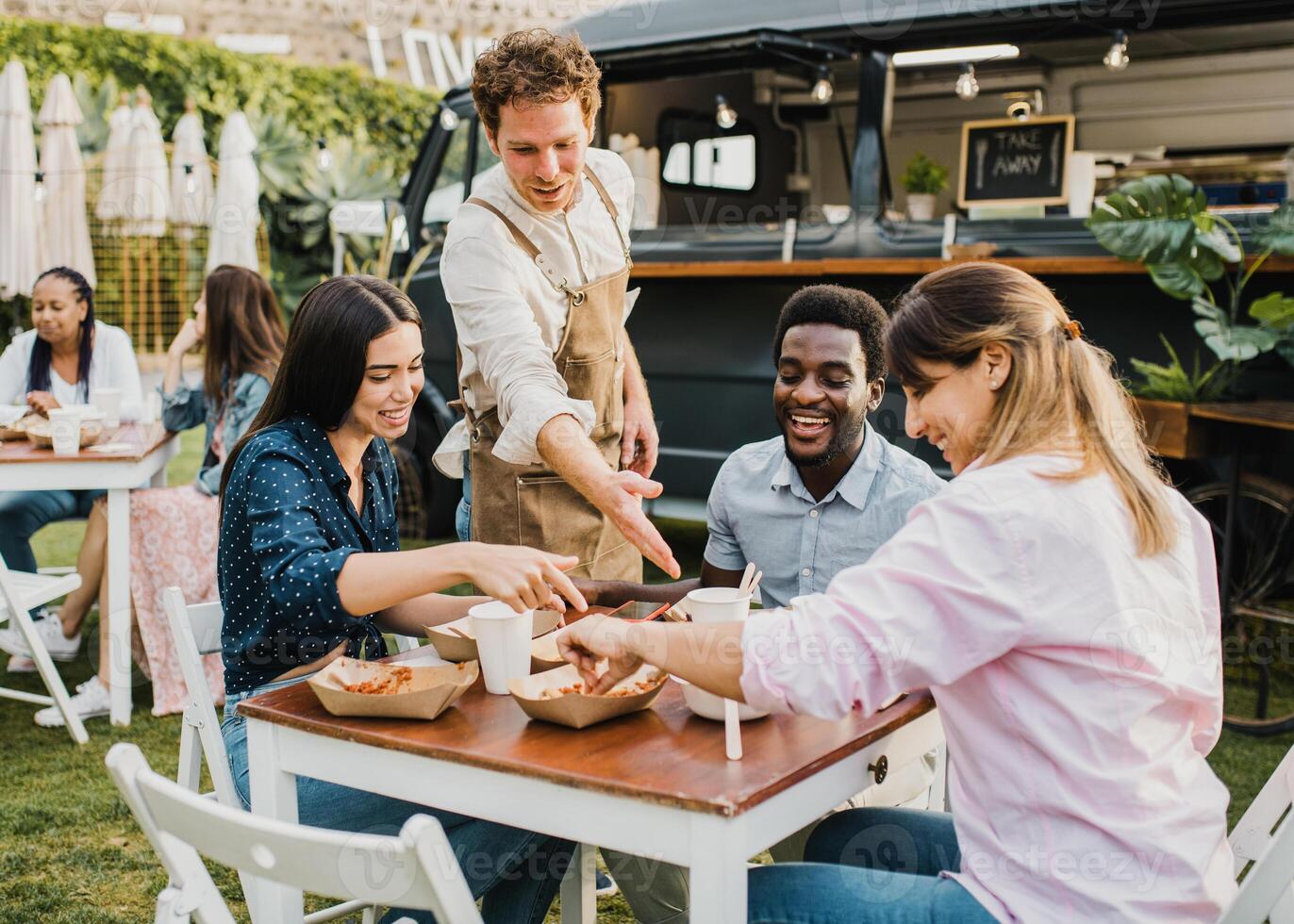 Multiracial people having fun eating at food truck outdoor - Focus on left girl face photo