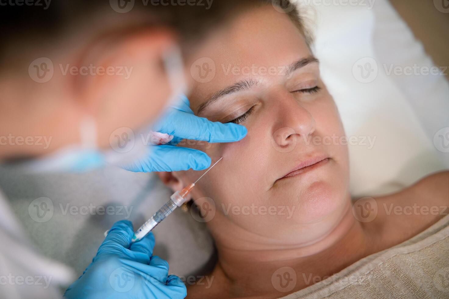 Faceless cosmetologist administering facial rejuvenating injection to client photo