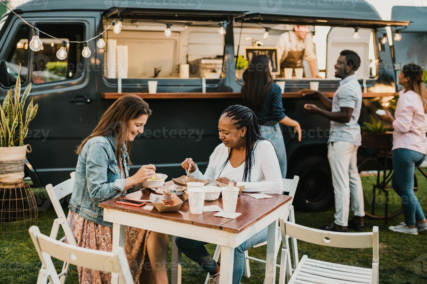 Diverse women having lunch in park near food truck photo