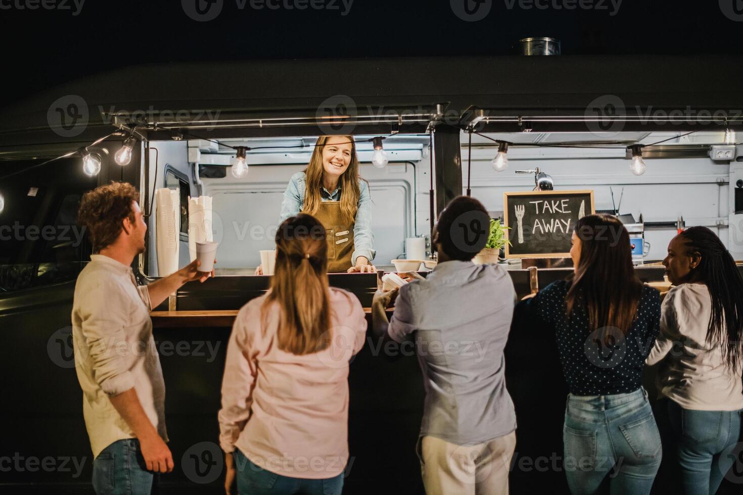 Diverse clients speaking with food truck seller at night photo