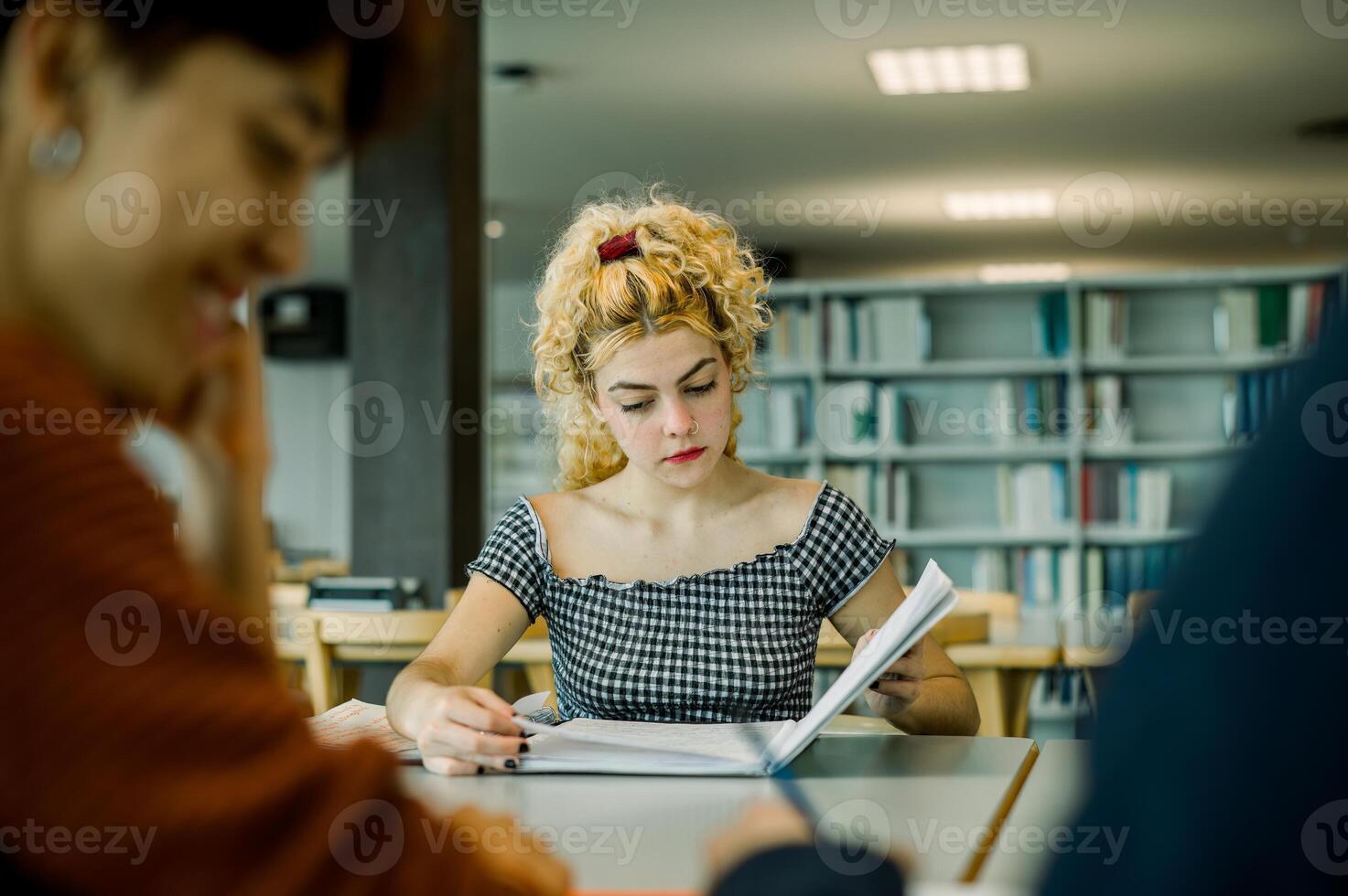 Focused woman reading book in library with crop ethnic student photo