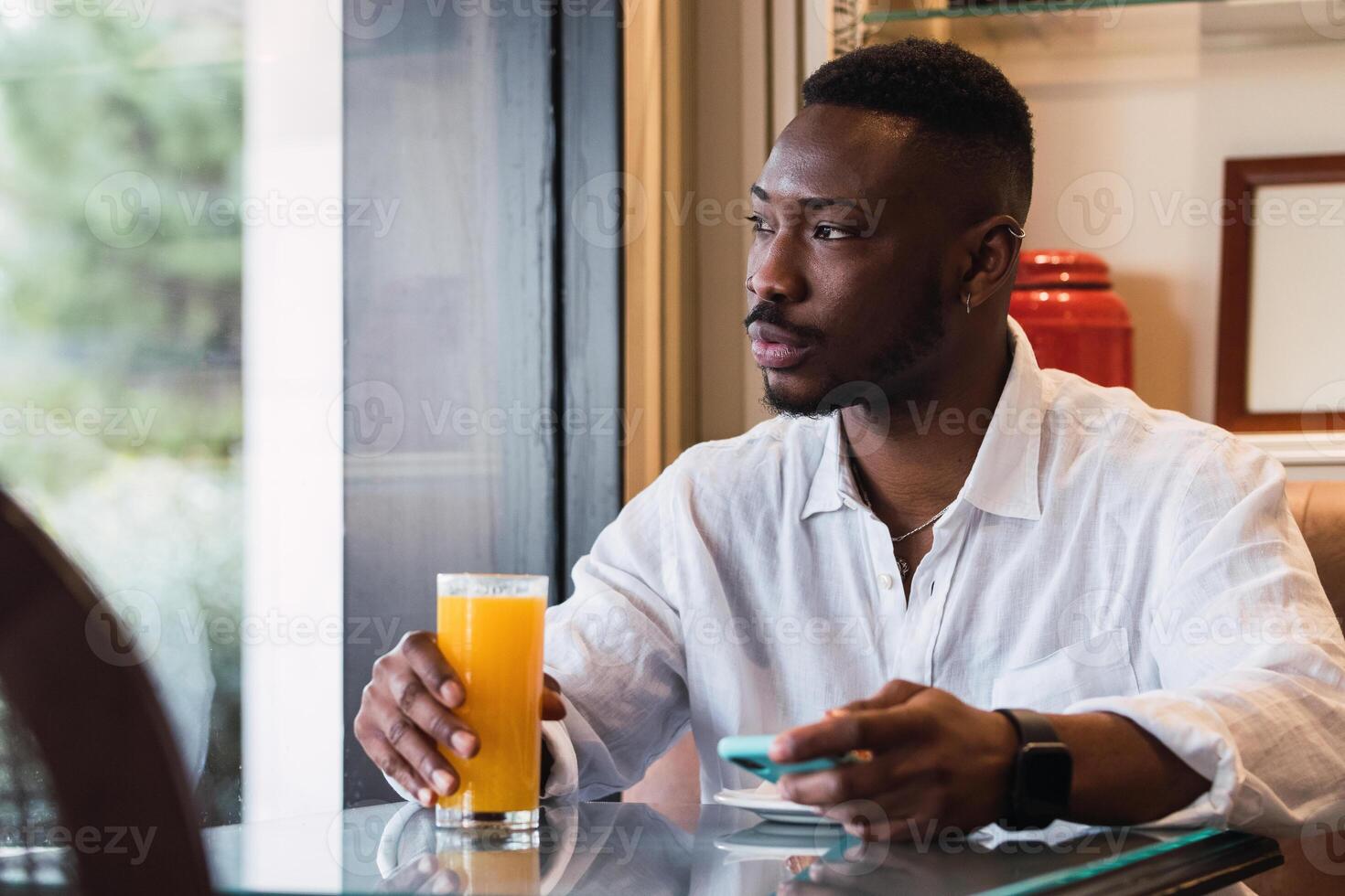 Serious black man using smartphone in cafe while sipping an orange juice photo