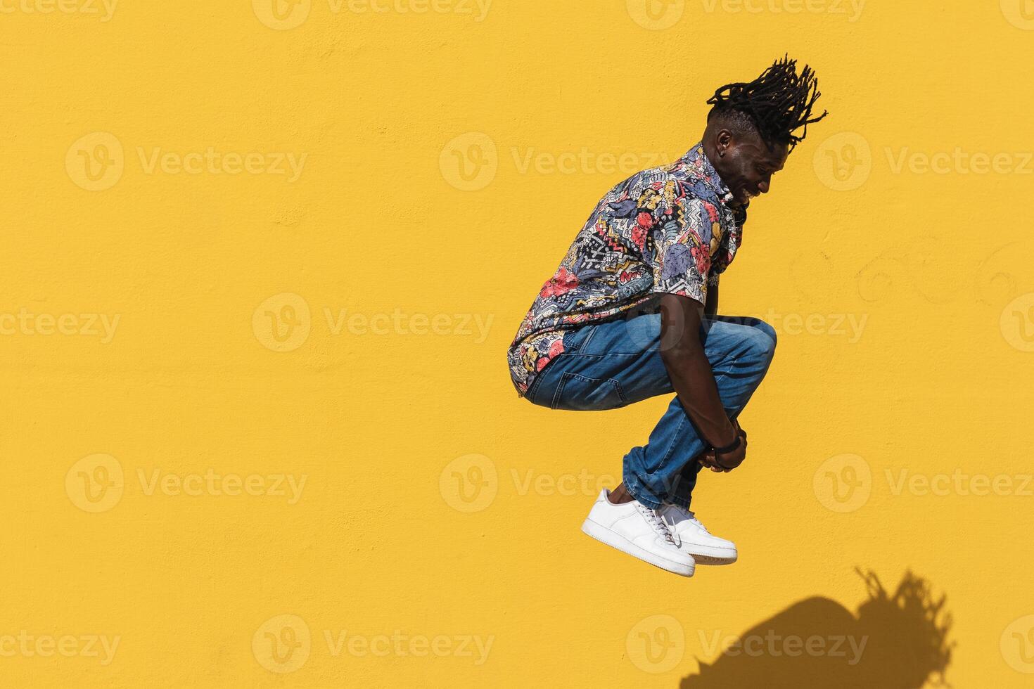 Energetic black man jumping near yellow wall photo