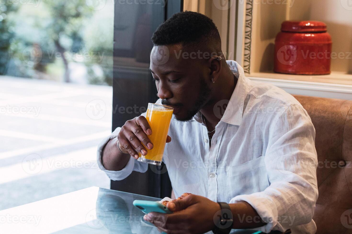 Black man browsing on phone in cafe while sipping an orange juice photo