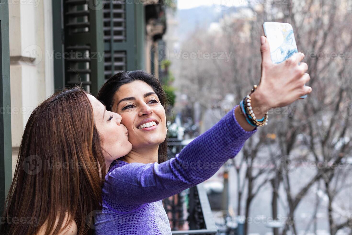 Happy ethnic lesbian couple taking selfie on balcony photo