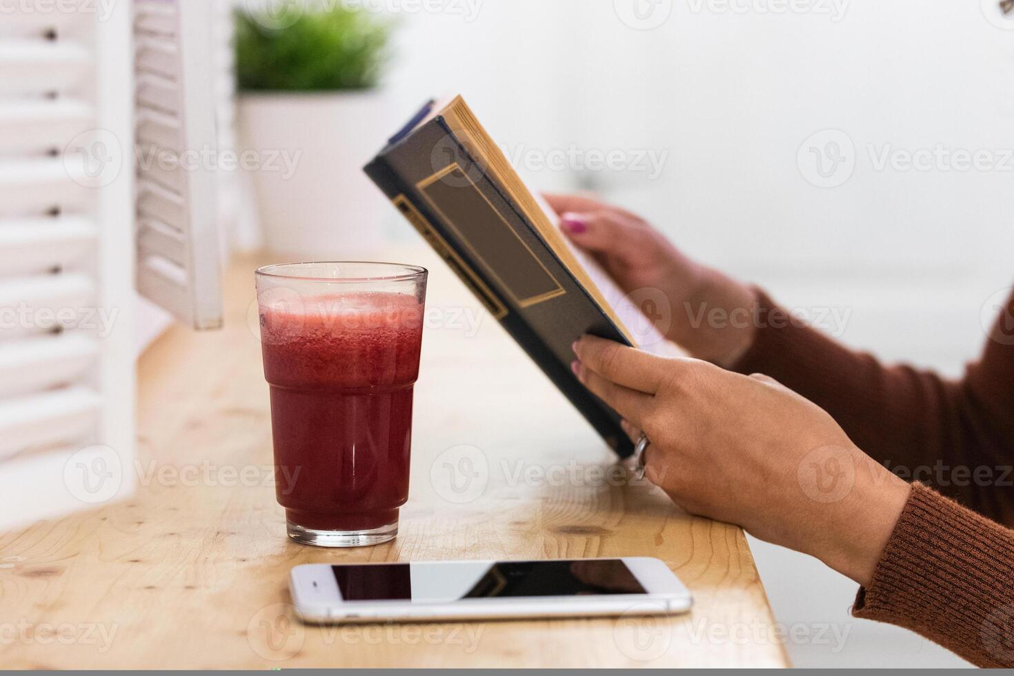 Anonymous African American woman drinking smoothie and reading book in bar photo