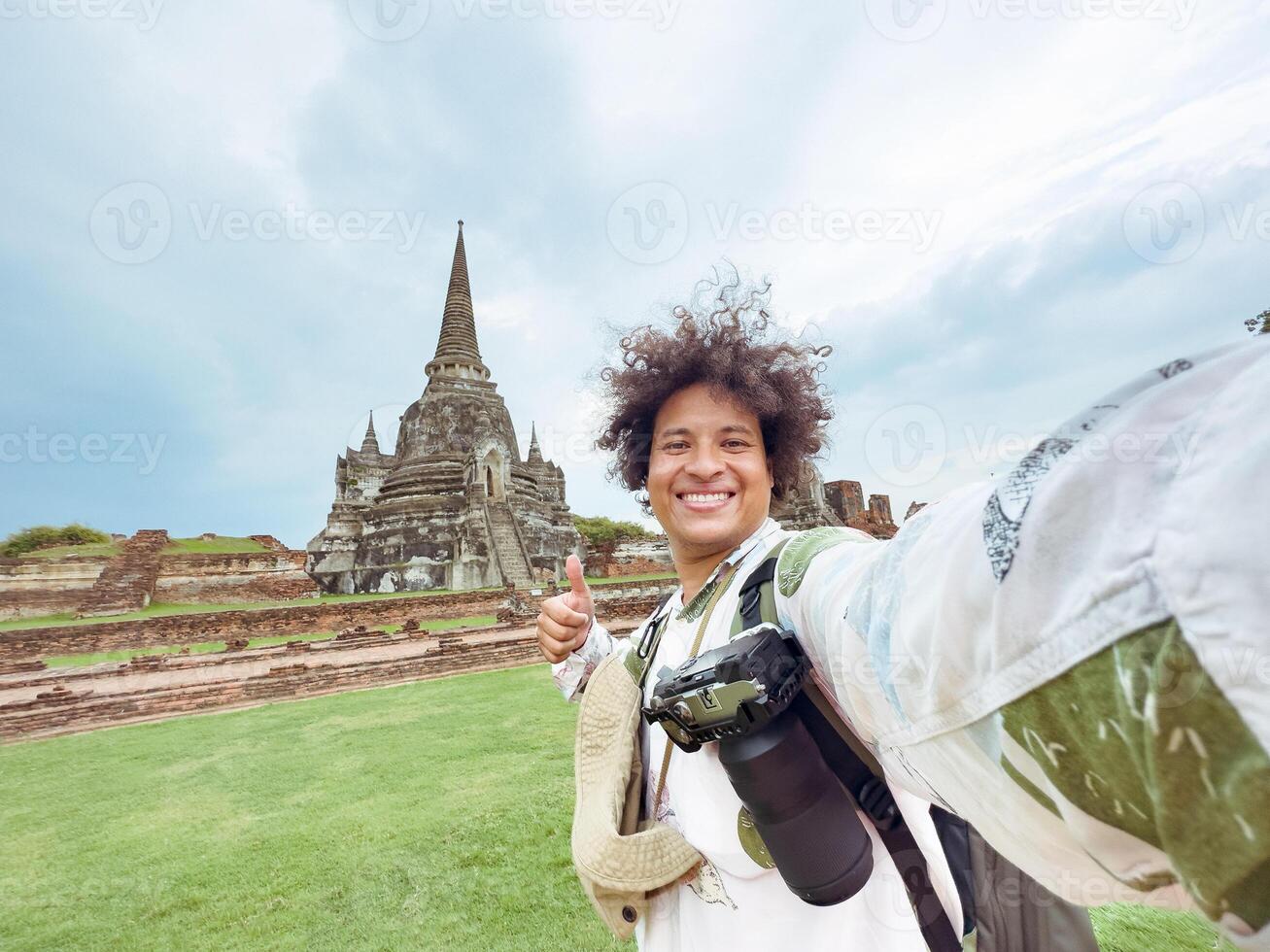 traveler with thumbs-up in front of towering Thai stupas, Enthusiastic Selfie at Ancient Thai temple photo