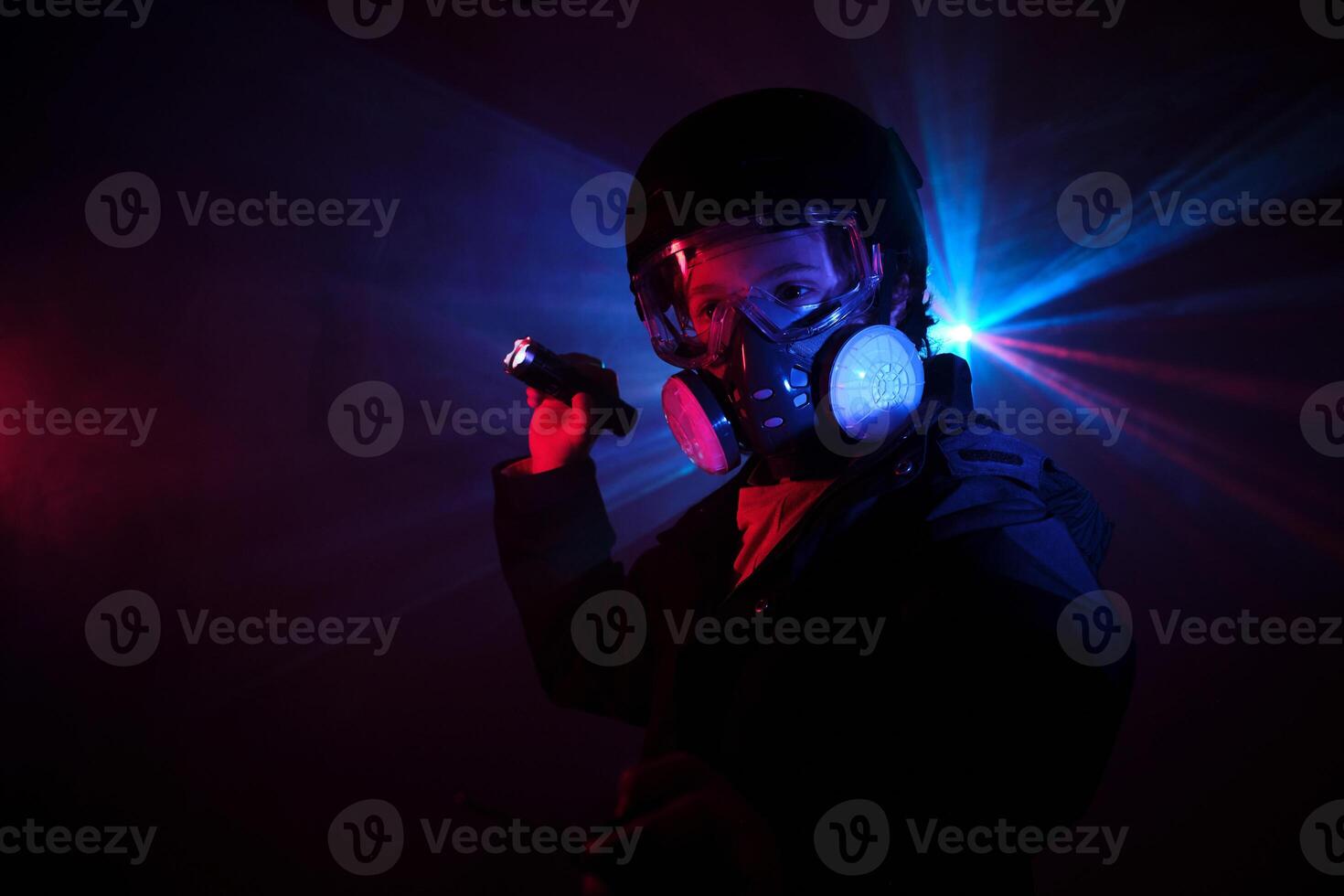 Kid in respirator shining flashlight in darkness photo