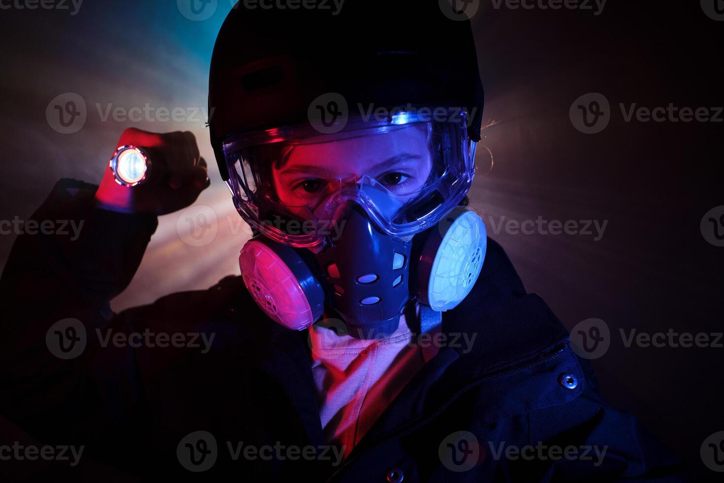 Boy in gas mask shining flashlight in dark studio photo
