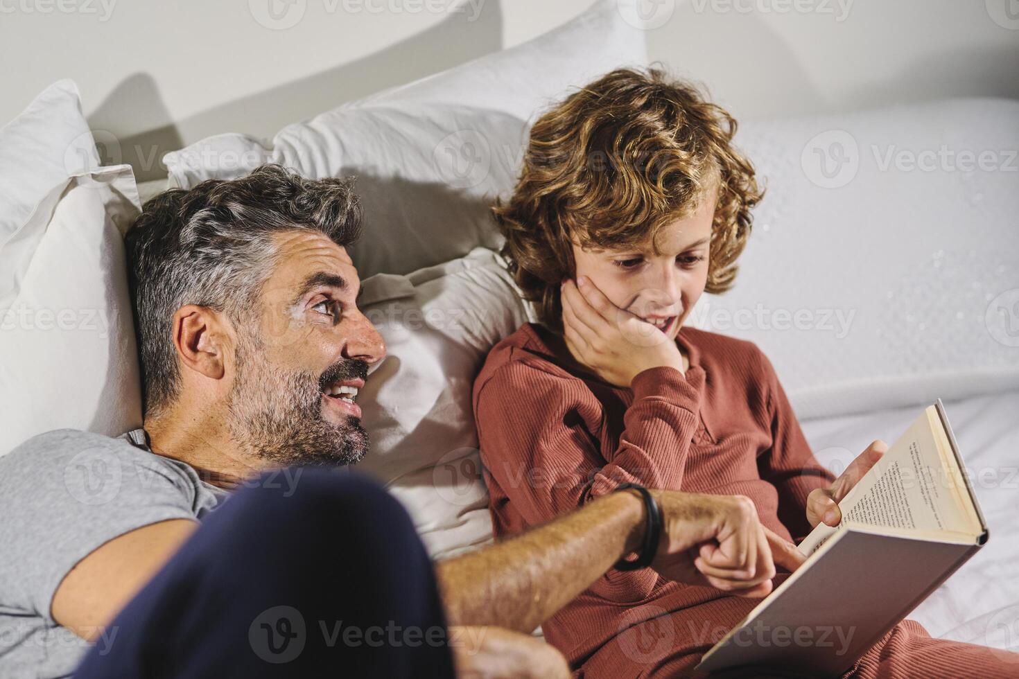 Father and son reading interesting book while lying on bed photo