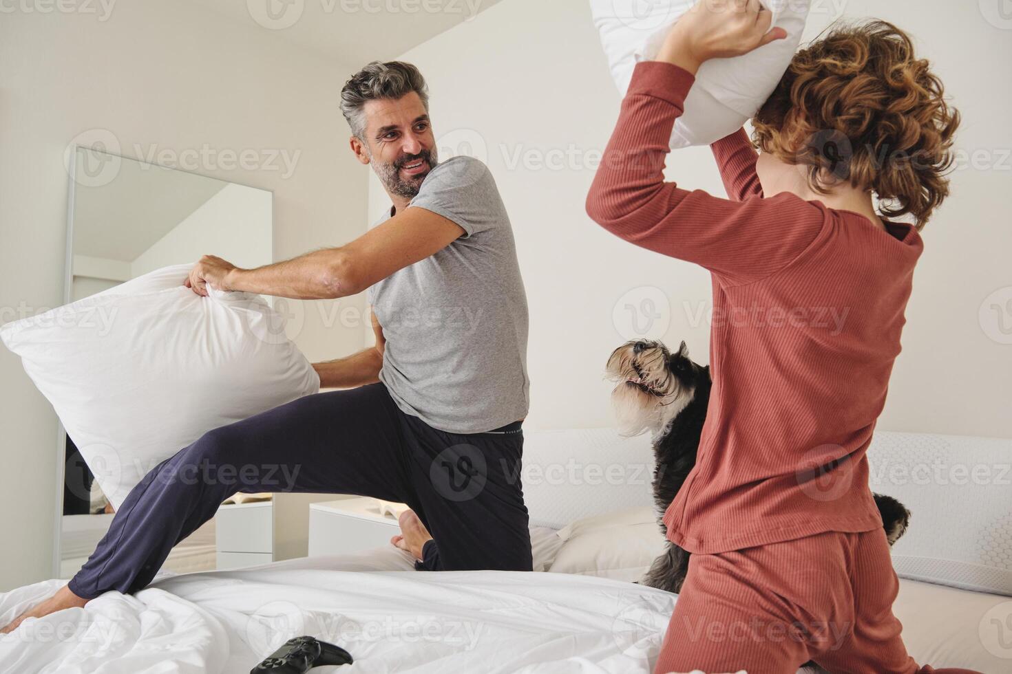 Happy man and boy fighting with pillows on bed photo