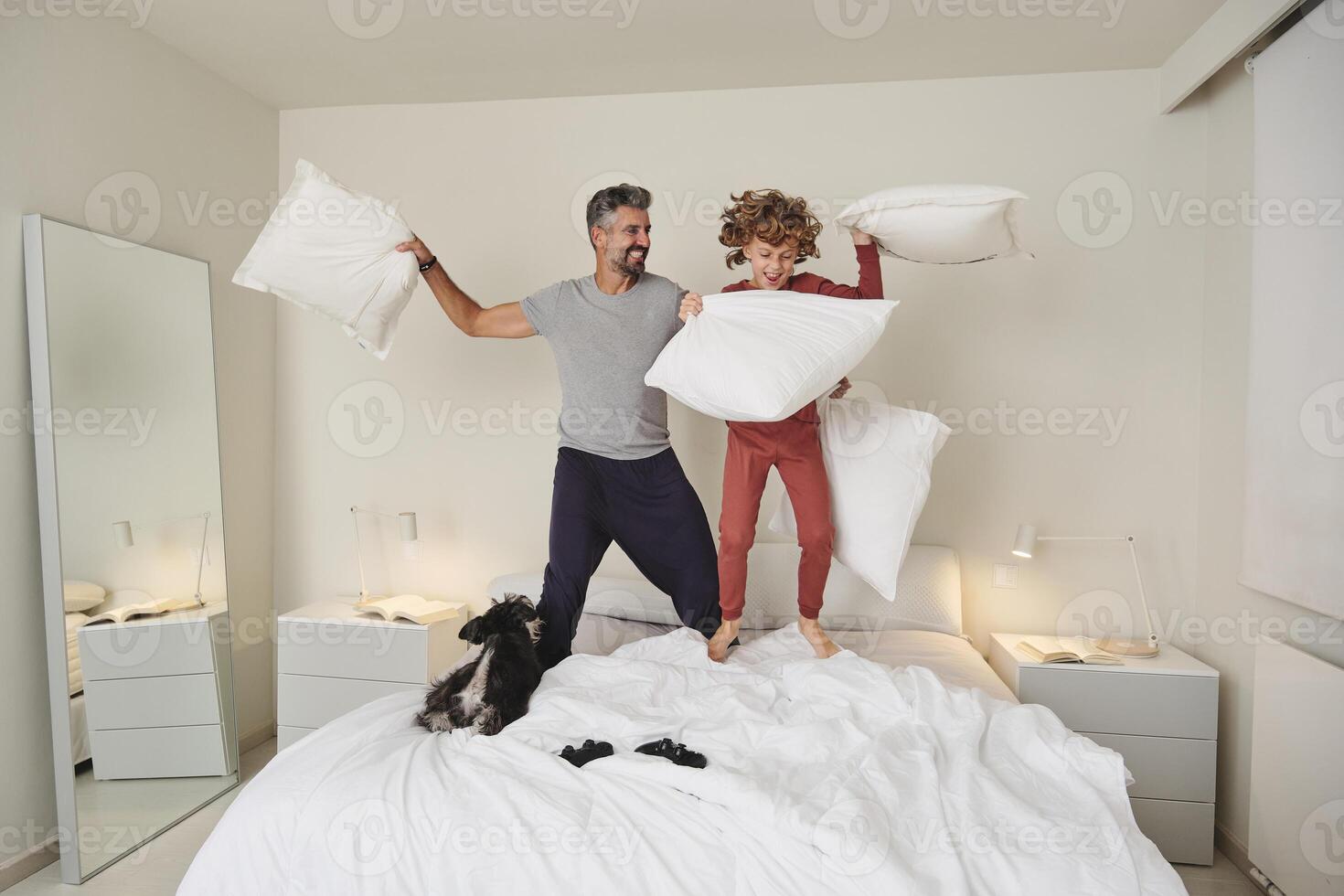 Playful man and kid fighting with pillows in bedroom photo
