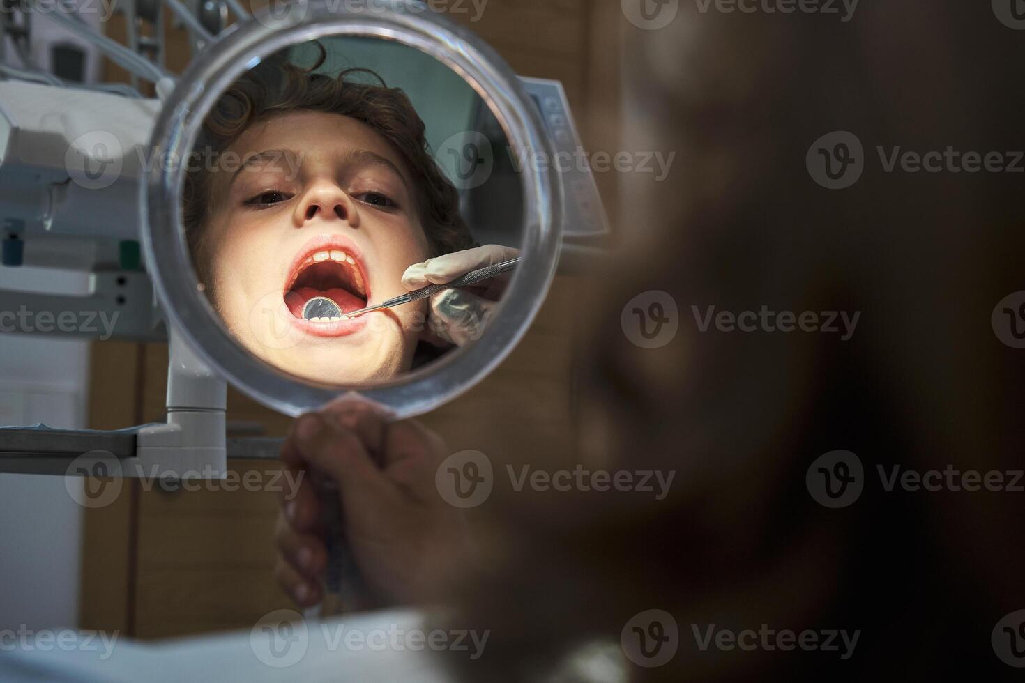 Dentist checking boy using mouth mirror in office photo