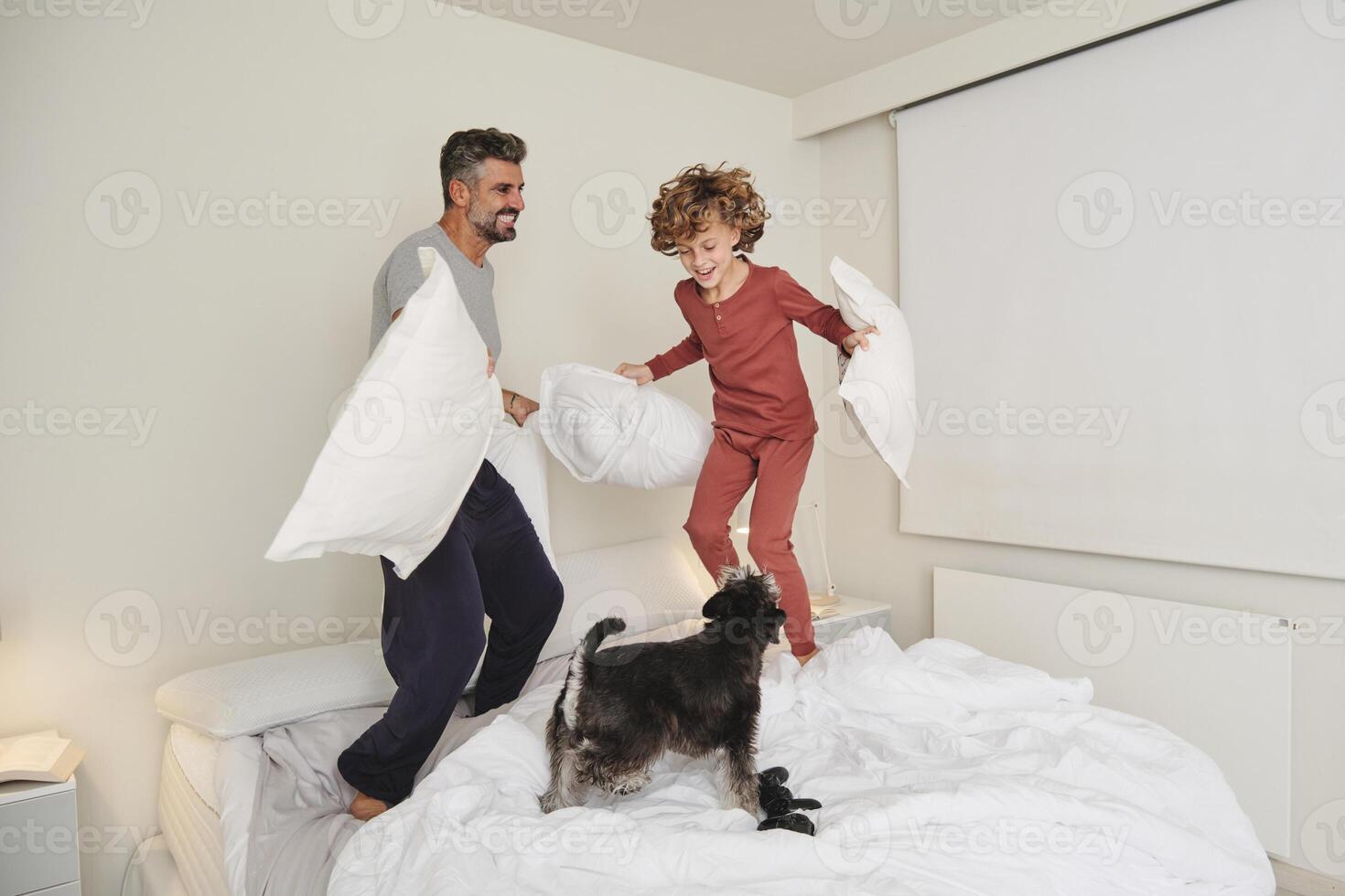 Smiling man and boy playing with dog on bed photo