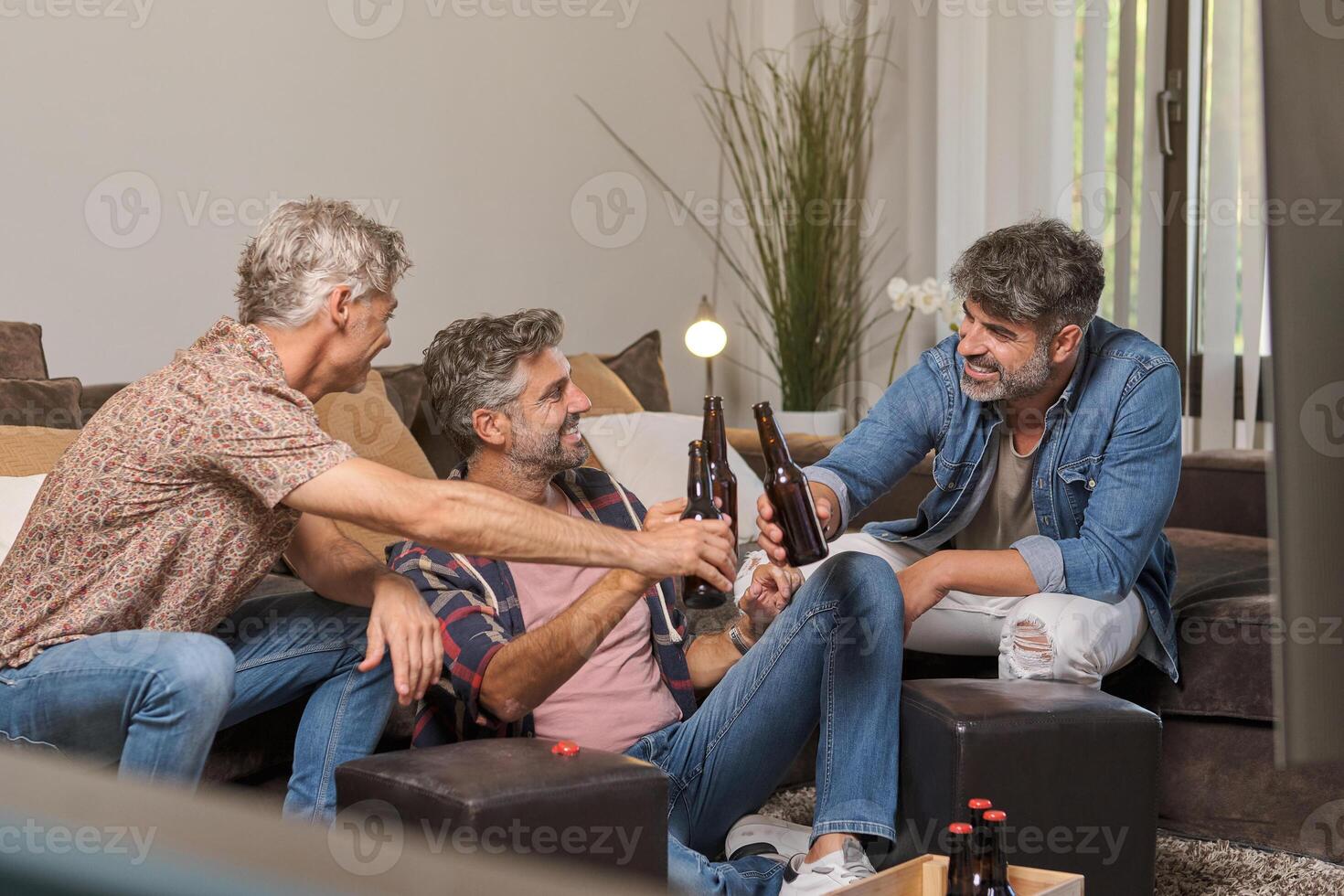 Father and mature sons clinking beer bottles and smiling at home photo