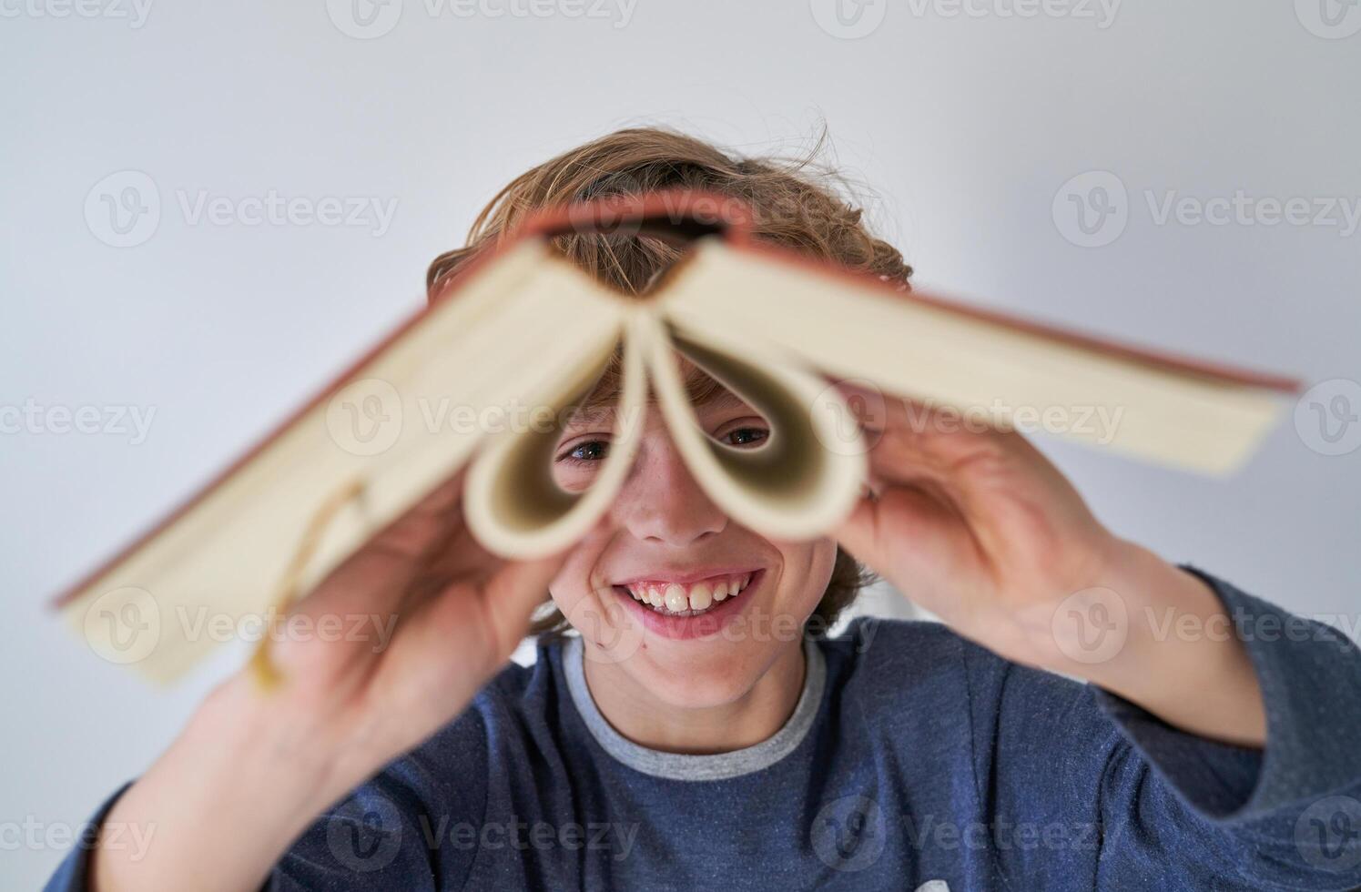 Cheerful boy looking at camera through opened book photo