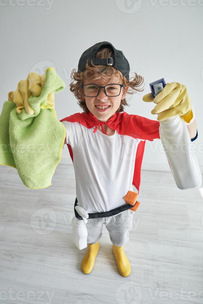 Smiling boy standing with house cleaning items and looking at ca photo