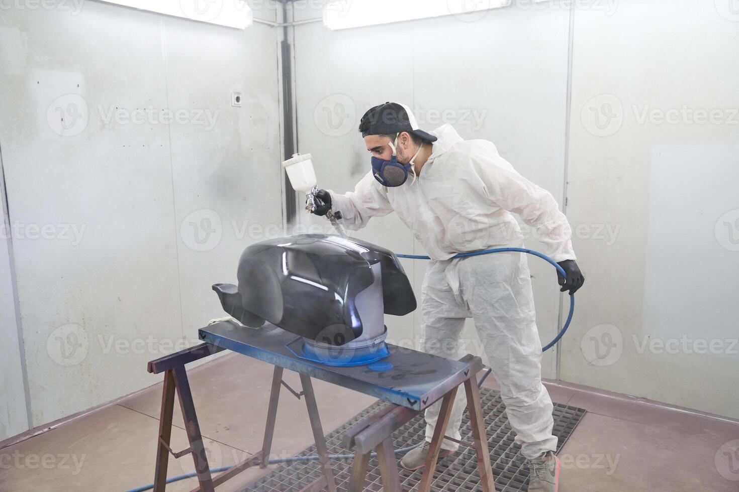 Man in dust suit painting motorbike tank in garage photo
