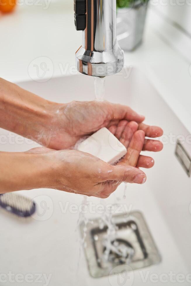 Person washing hands with soap under water in sink photo