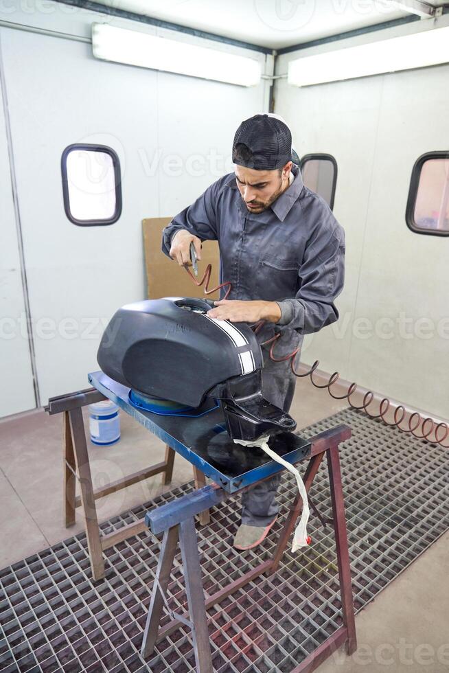 Male mechanic painting motorcycle tank in workshop photo