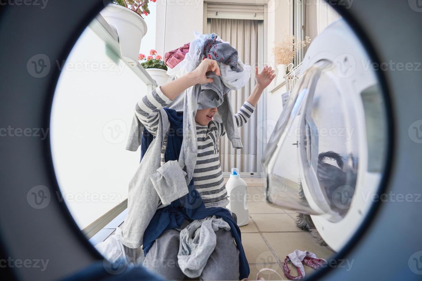Boy playing with clothes in laundry room photo