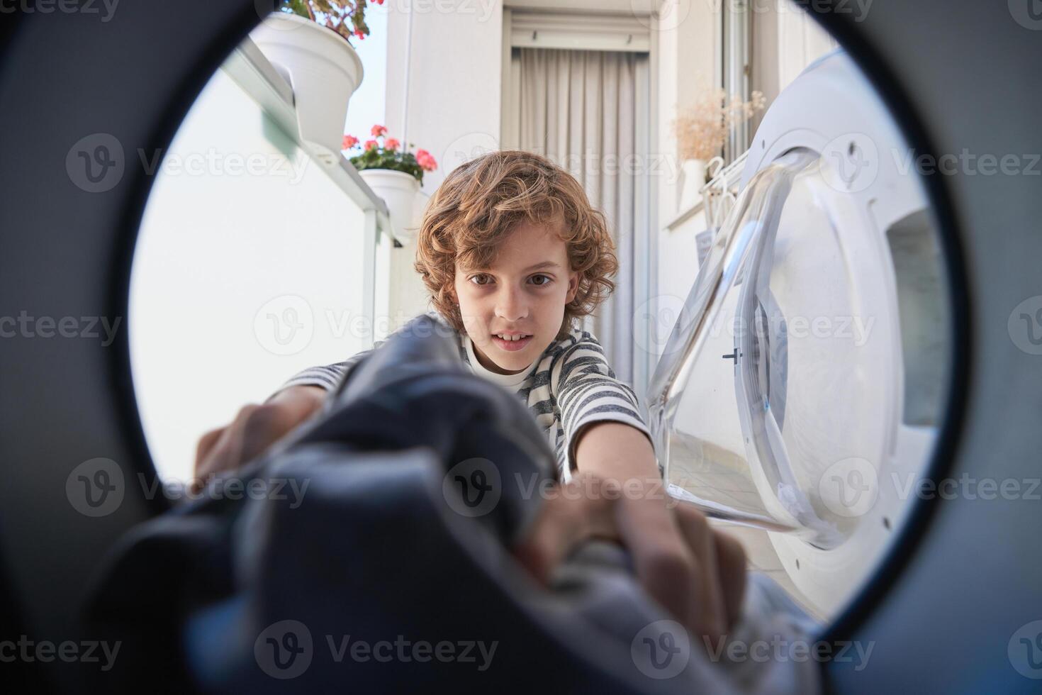 Positive kid taking clothes out of washing machine photo