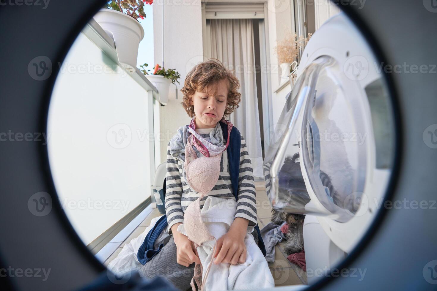 Upset boy with dirty clothes sitting near washing machine photo