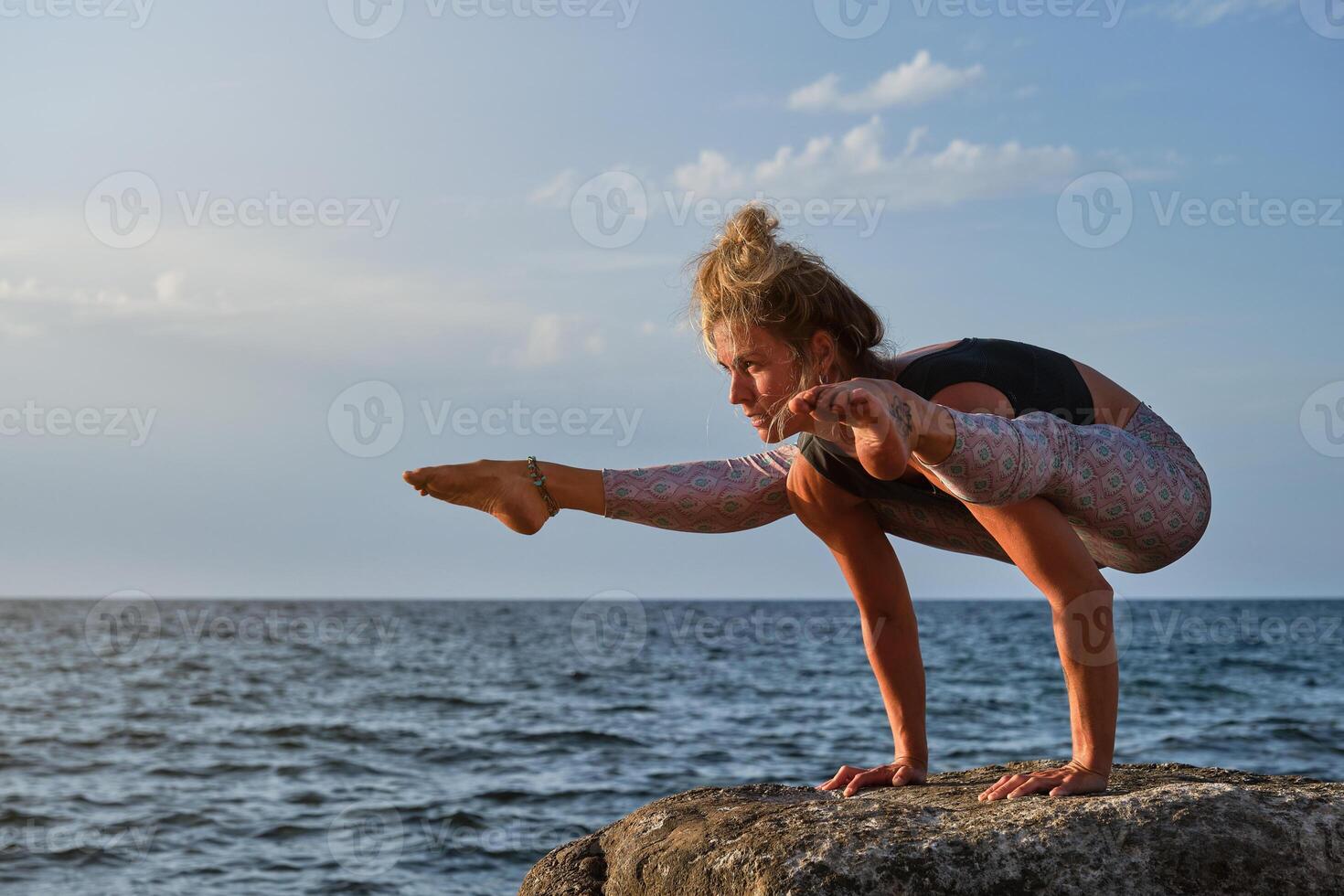 Fit woman balancing on arms while practicing yoga asana on stone photo