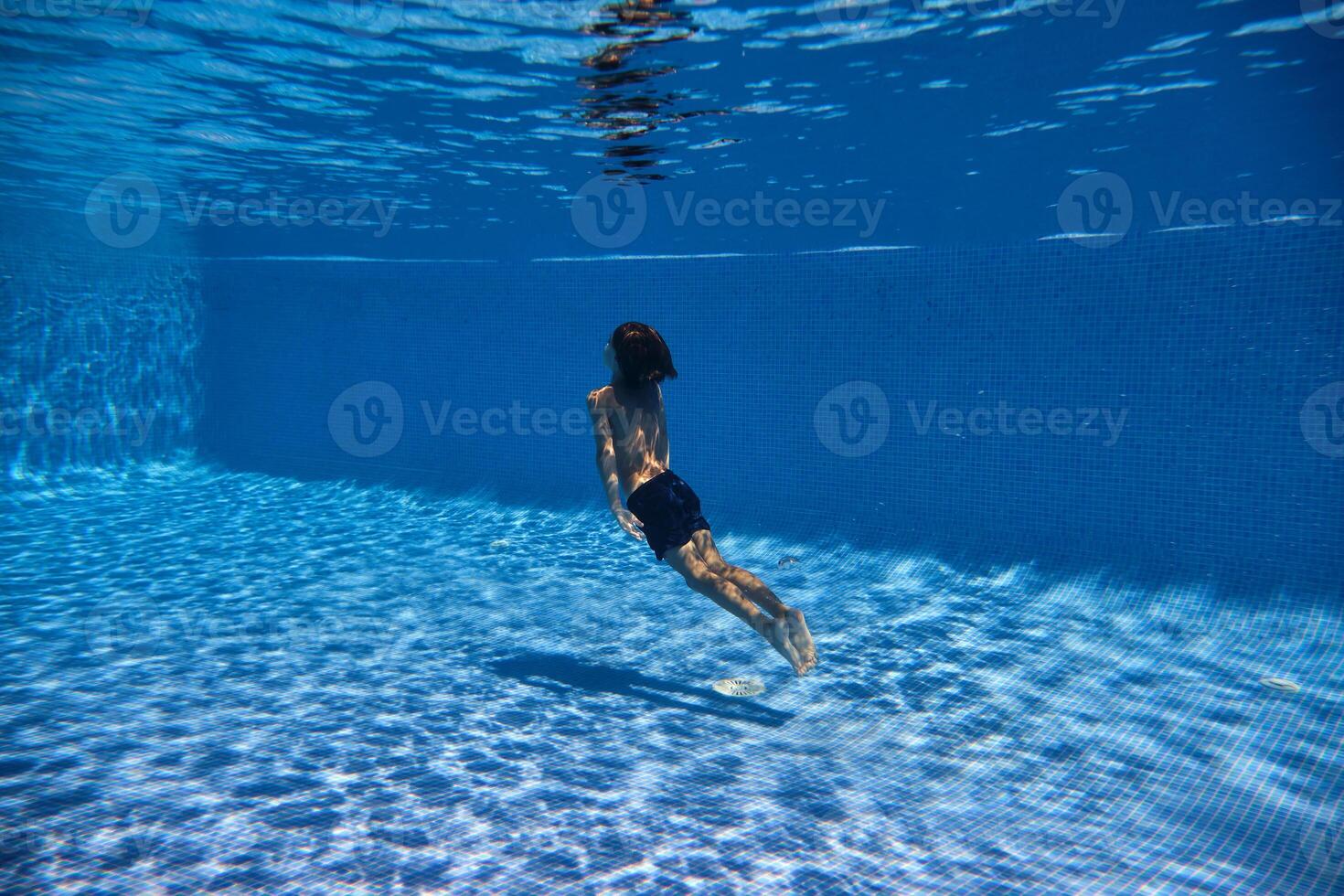 Boy swimming towards surface of tiled pool photo