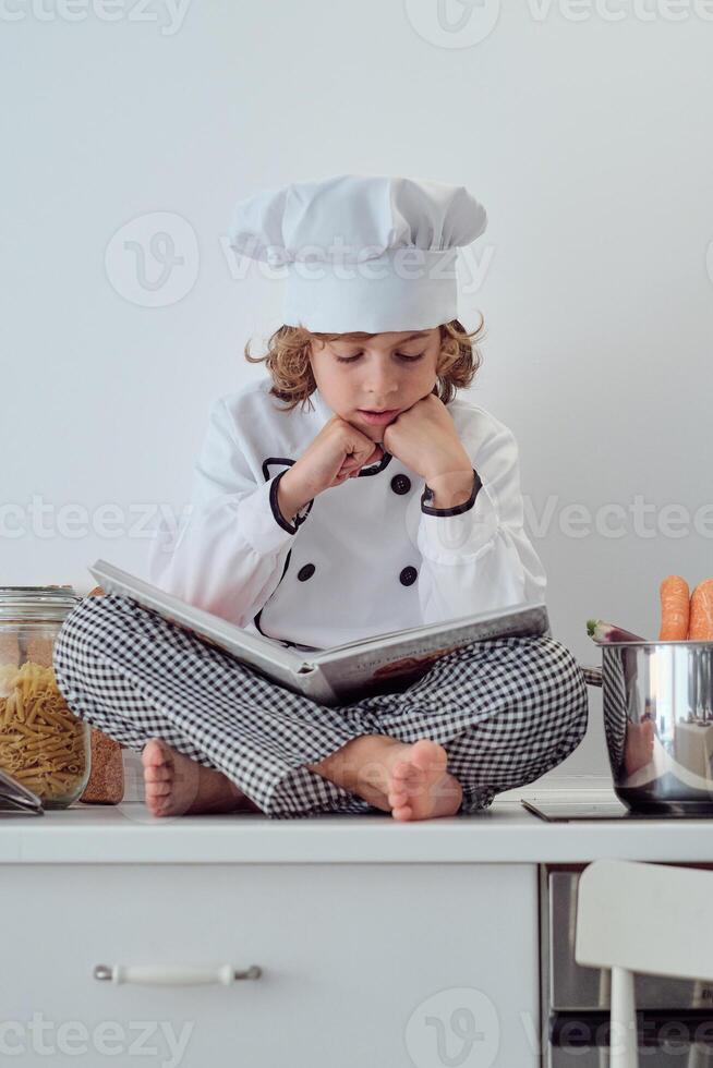 Attentive preteen boy in chef costume reading culinary book photo