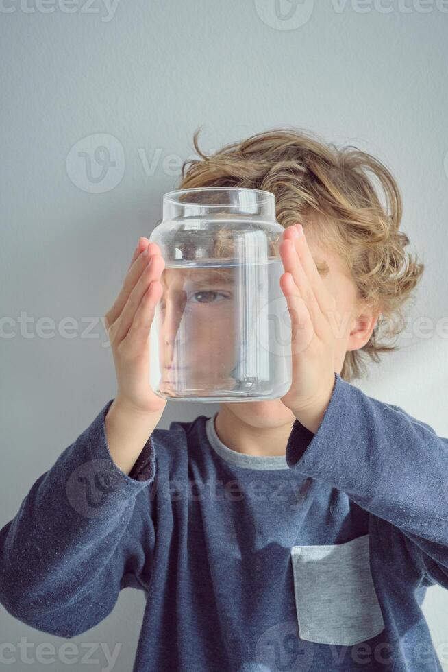 Kid covering face with jar of water photo