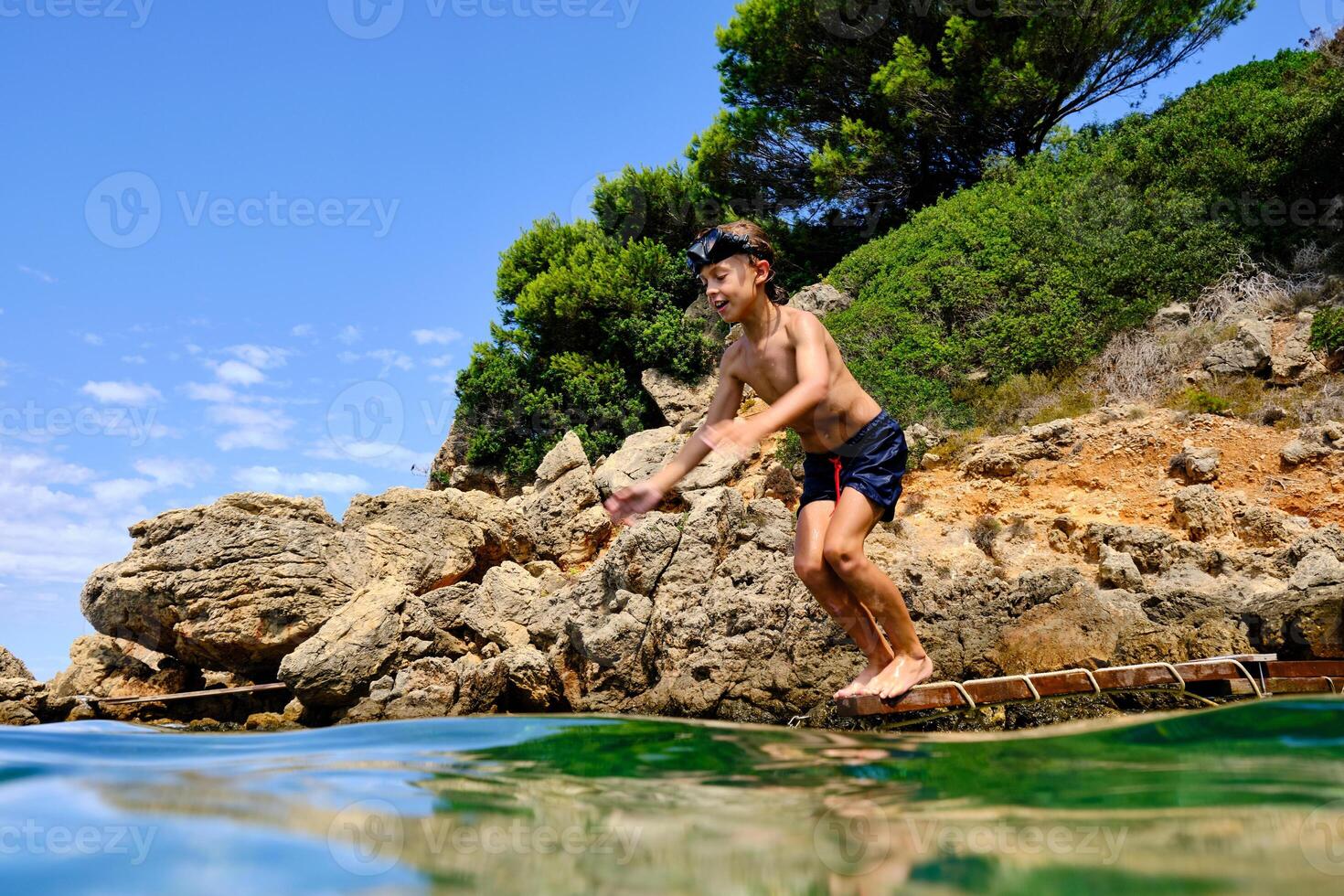 Shirtless boy diving into water from wooden plank photo