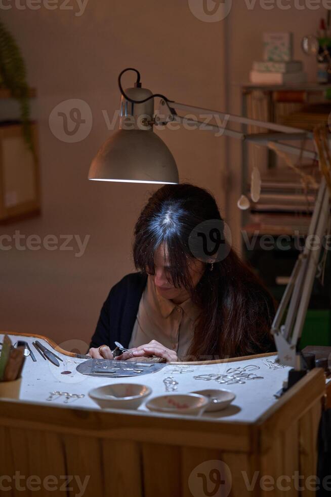 Focused female goldsmith using rotative tool while creating jewe photo