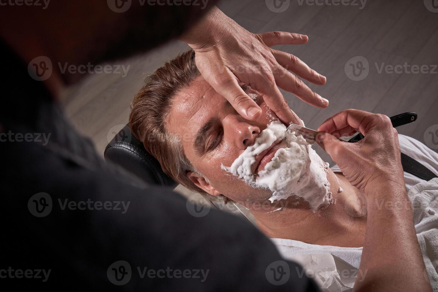 Anonymous man shaving beard of client photo
